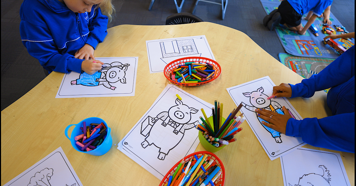 two children colouring in pigs with crayons